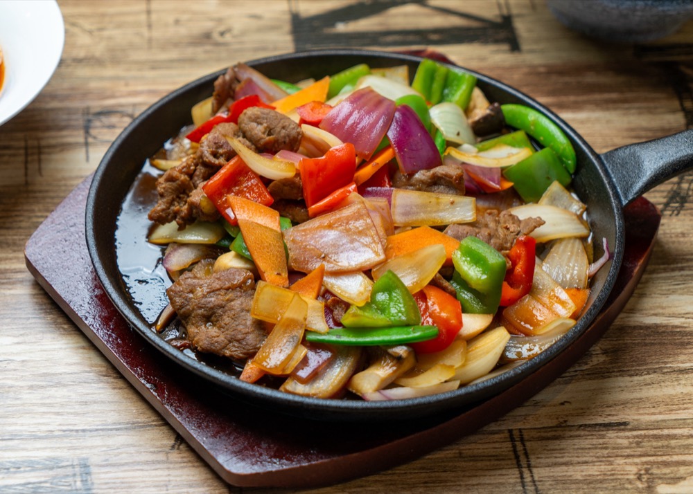 Stir-fried meat and peppers on a sizzling iron plate